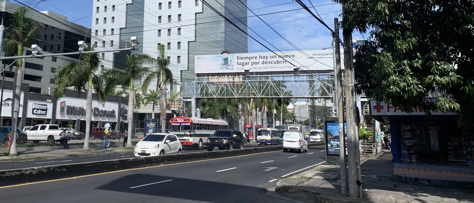 Tráfico y palmeras en la Alameda Roosevelt de San Salvador, con una pasarela peatonal sobre la avenida