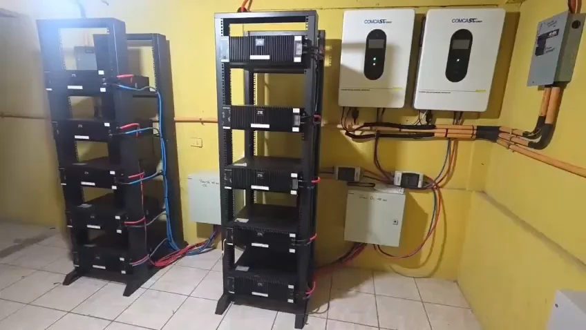 Dos inversores híbridos Comcast Energy montados en muro, con dos racks de módulos de batería y su canalización eléctrica